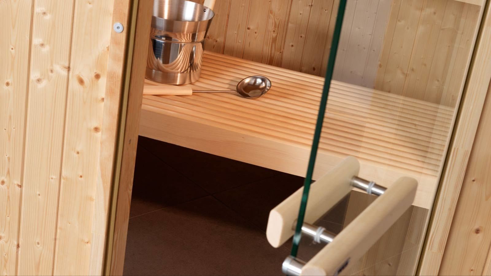 A wooden sauna room with a metal bucket, a wooden bench, and a metal handle.