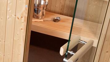 A wooden sauna room with a metal bucket, a wooden bench, and a metal handle.