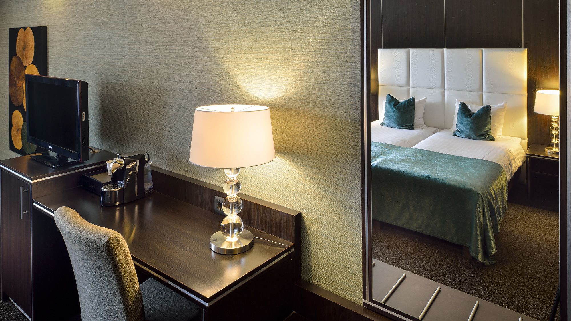 Habitación de hotel con escritorio, lámpara, cama con cubrecama verde y un espejo grande.