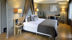 A modern hotel room with a large bed, bedside lamps, a desk, and a potted plant.