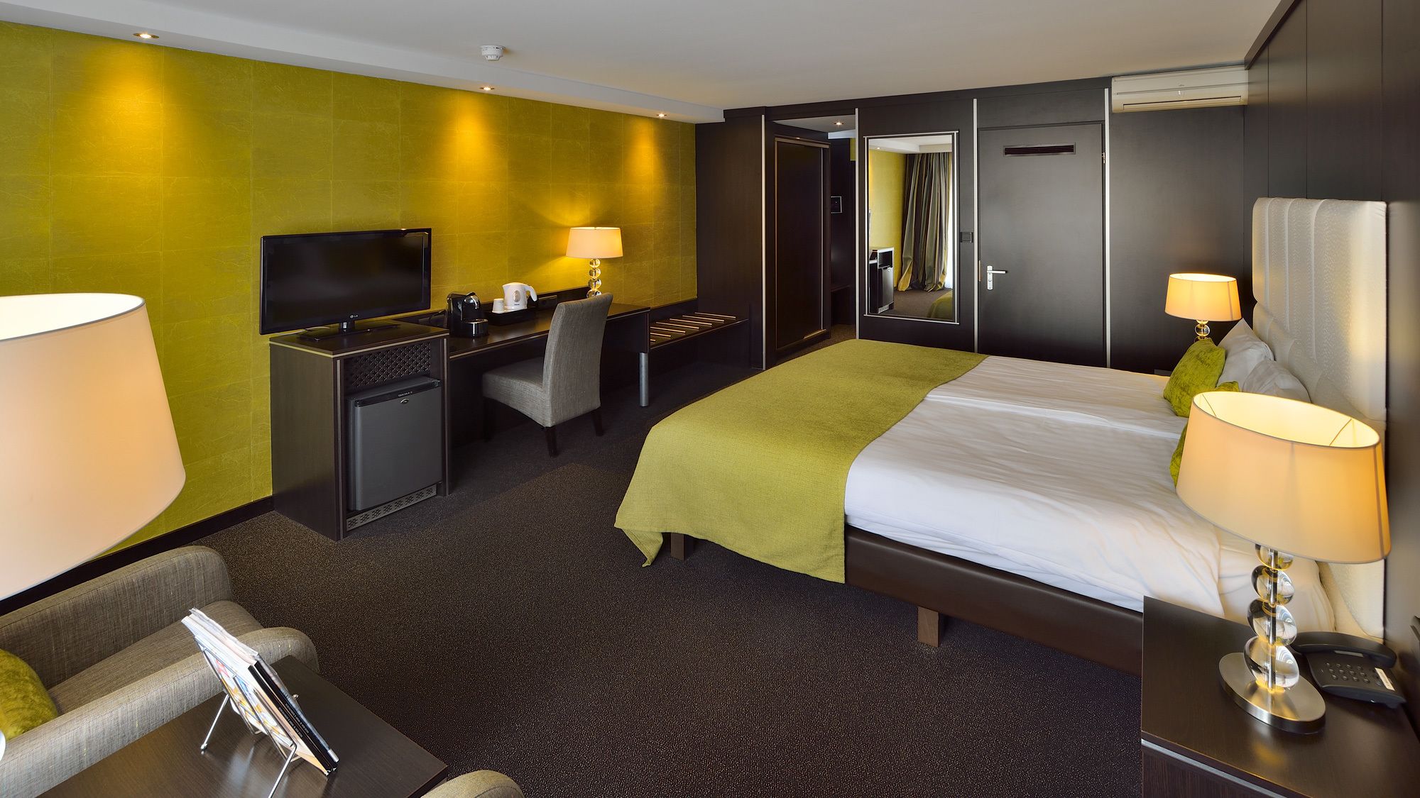 A hotel room with a bed, desk, chair, TV, and a small fridge.