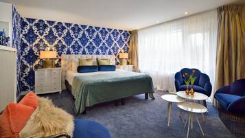Une chambre d’hôtel avec un lit, une table de chevet, une chaise, une petite table et une fenêtre avec des rideaux.