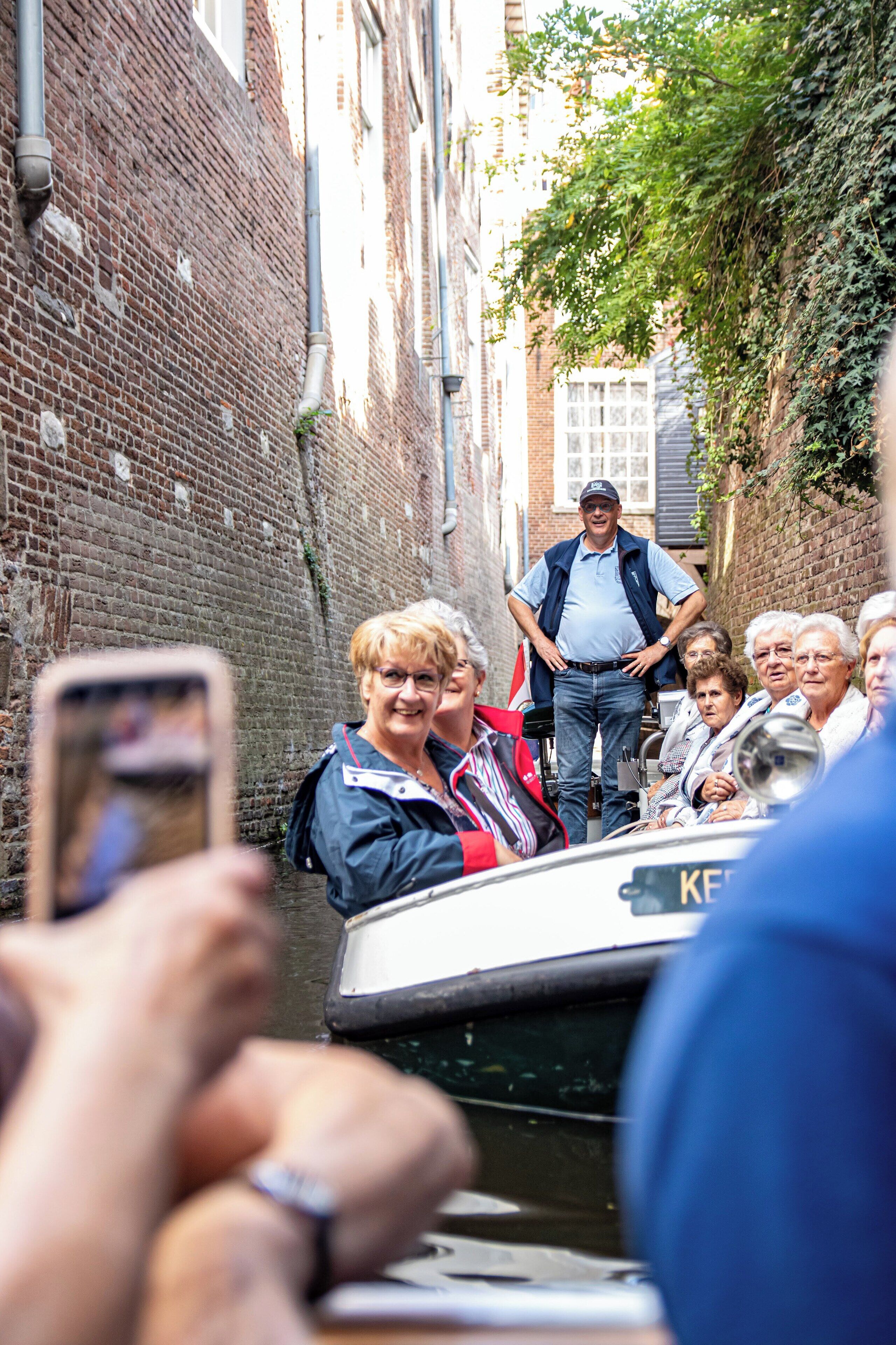 A narrow canal with a boat, brick buildings, and a crowd of people.