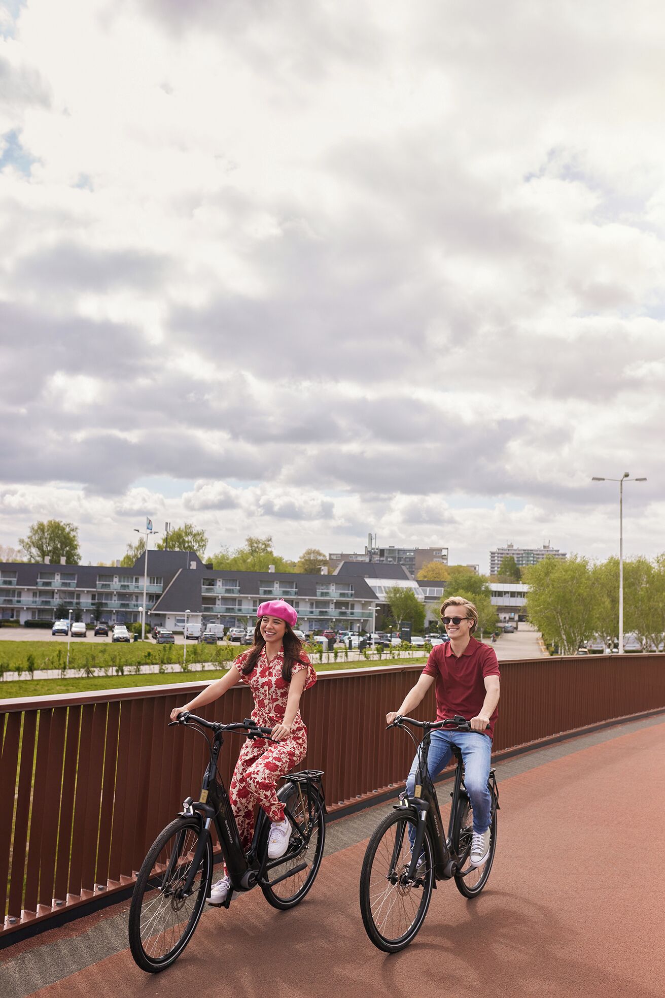 Two people riding bicycles on a bridge with a cityscape in the background.