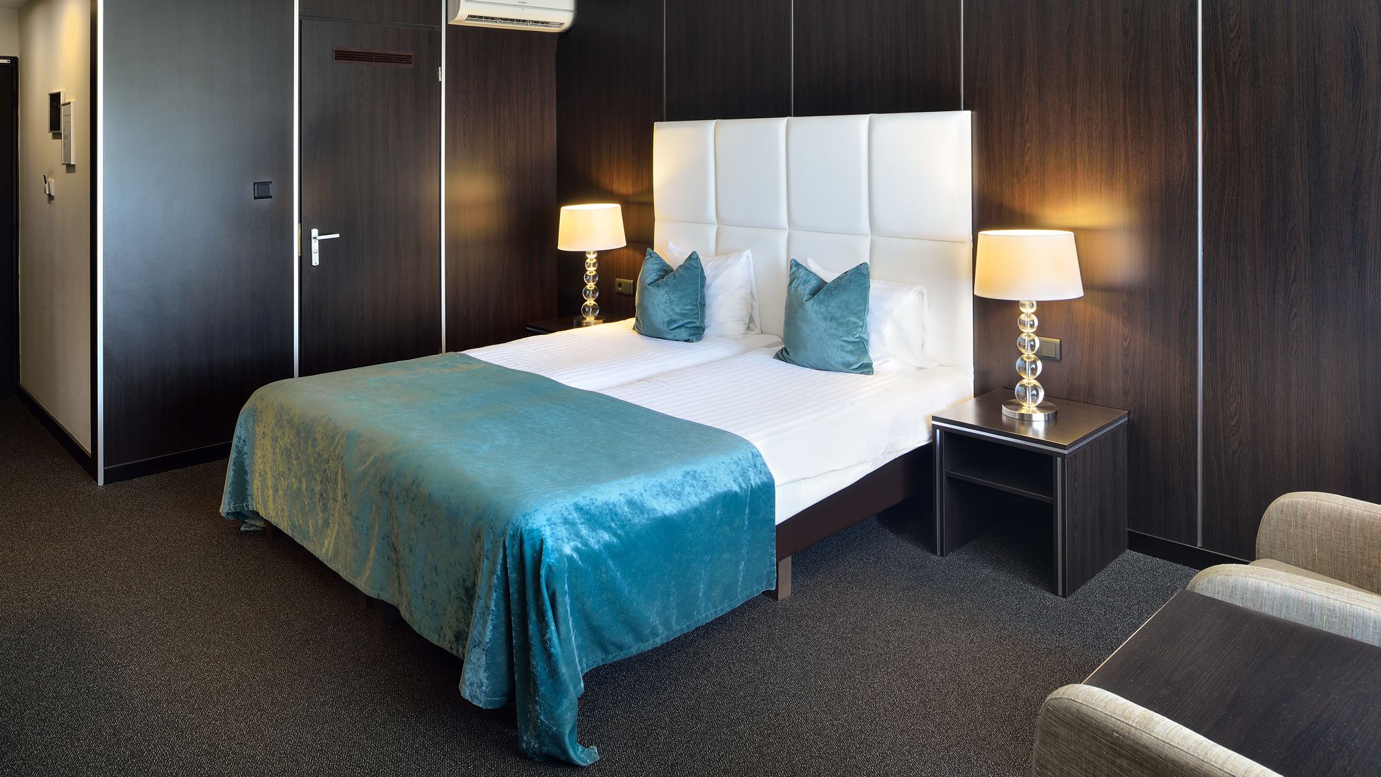 Habitación de hotel con una cama grande, dos lámparas de noche, una mesita de noche y una silla.