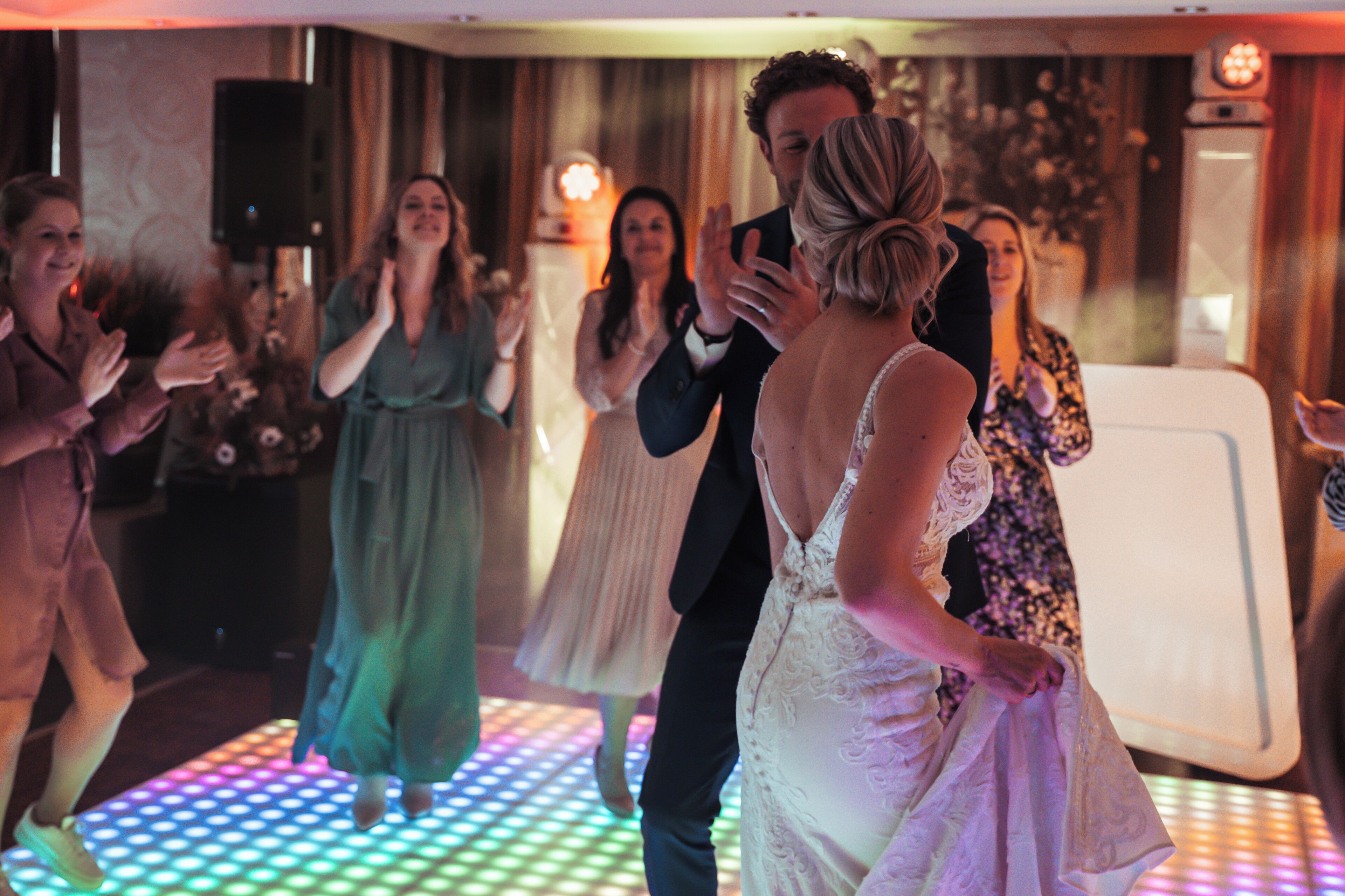 A wedding reception with guests dancing on a lit dance floor.