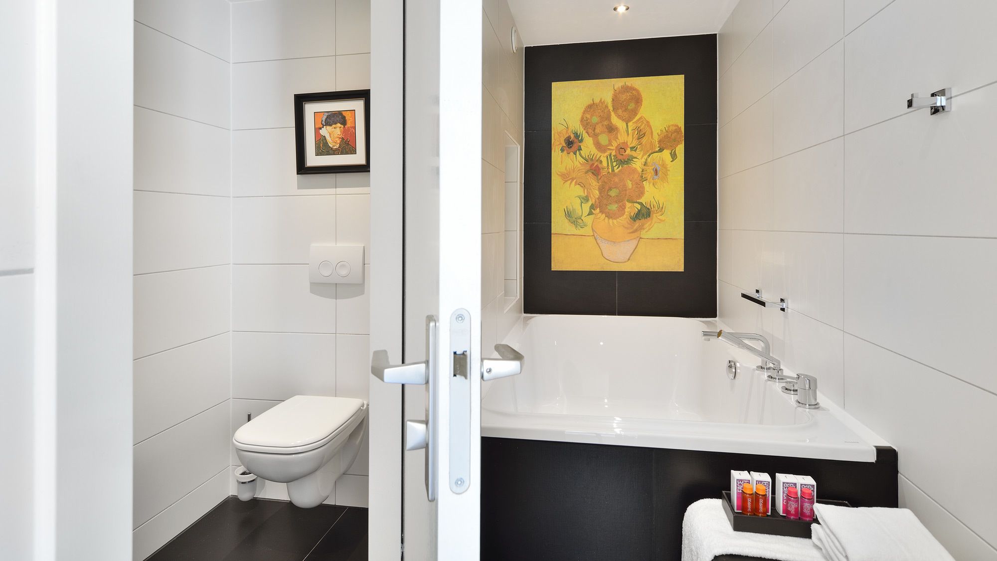 A modern bathroom with a white toilet, a large sink, and a framed painting above the sink.