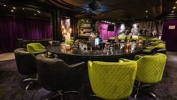 A conference room with a round table, green and black chairs, a bar area, and purple curtains.