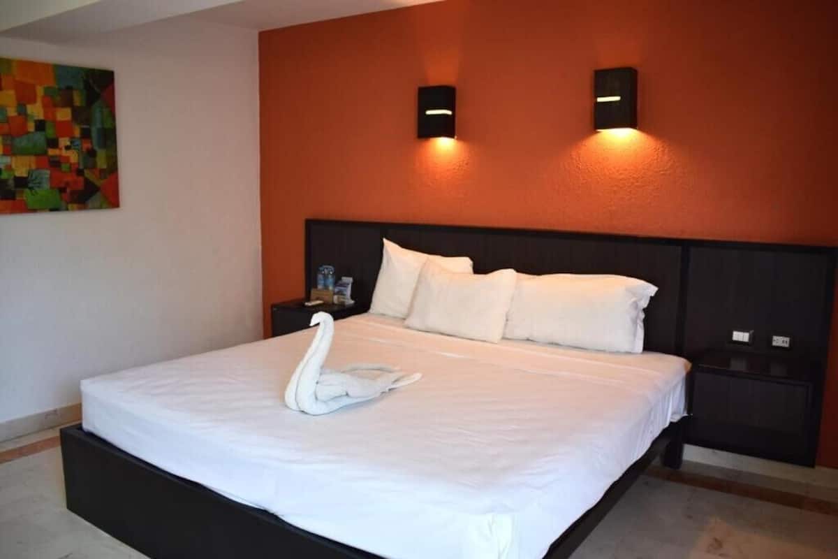 Un lit bien fait, agrémenté d’un oreiller en forme de cygne, d’une tête de lit noire et de deux lampes fixées au mur.