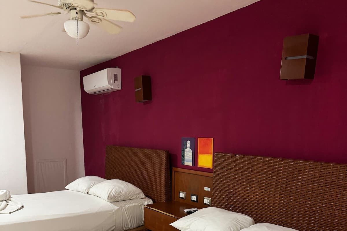 Une chambre d’hôtel avec deux lits, un ventilateur de plafond, un appareil de climatisation et un luminaire fixé au mur.