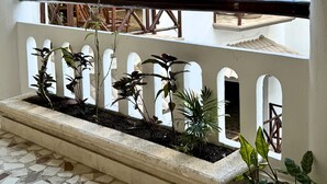 Um pátio com piso de azulejos, guarda-corpo branco e um jardineiro com diversas plantas.