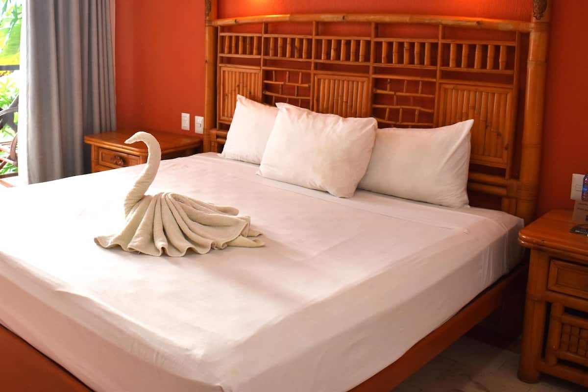 Une chambre d’hôtel avec un lit, une tête de lit en bois, une table de chevet et une fenêtre avec des rideaux.