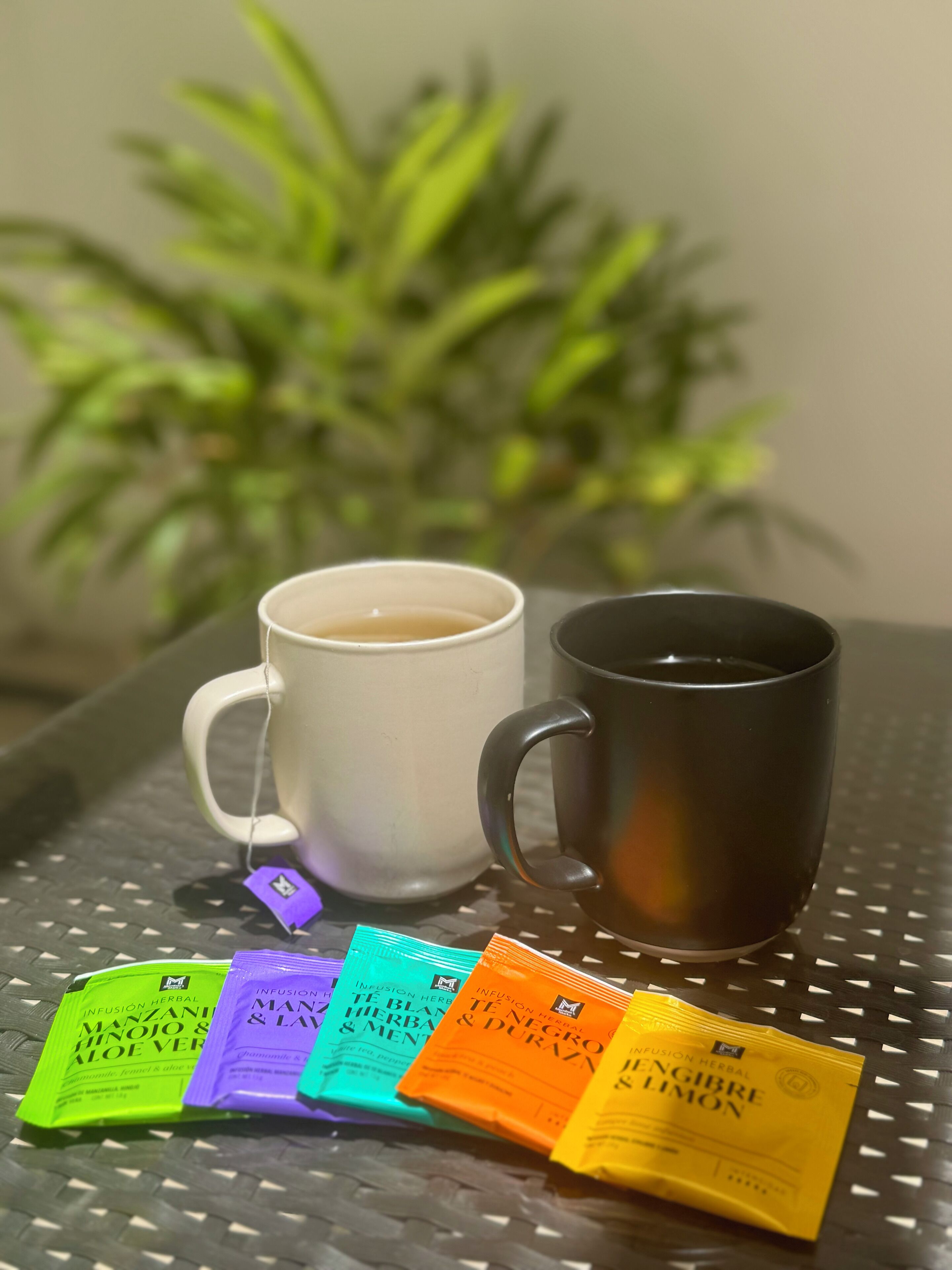 A tray with two cups of coffee, a plant, and several herbal tea packets.