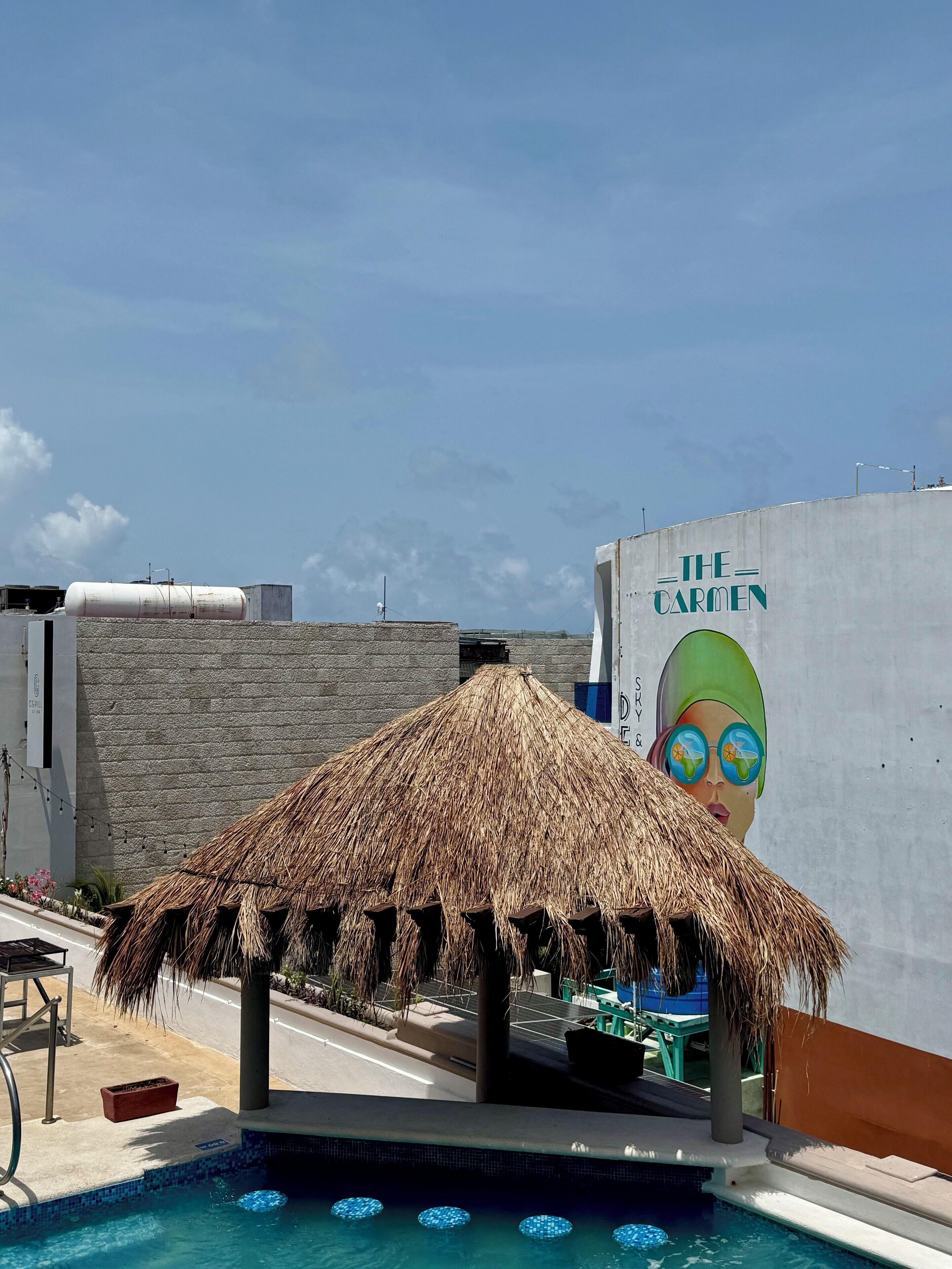 Un área de piscina con una sombrilla de paja, una silla de descanso y una pared con un mural.