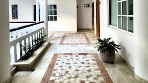 Um corredor com piso de azulejos, paredes brancas e um vaso de planta.