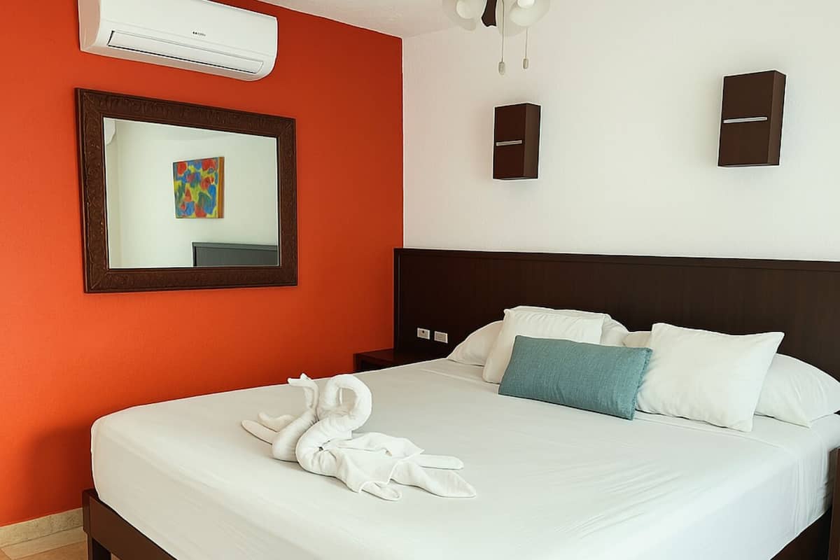 Une chambre d’hôtel avec un grand lit, du linge de lit blanc, une œuvre d’art encadrée au mur et un climatiseur fixé au mur.