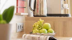 Una encimera de cocina con un hervidor, un bol de fruta y un libro rojo titulado 'Mates'.