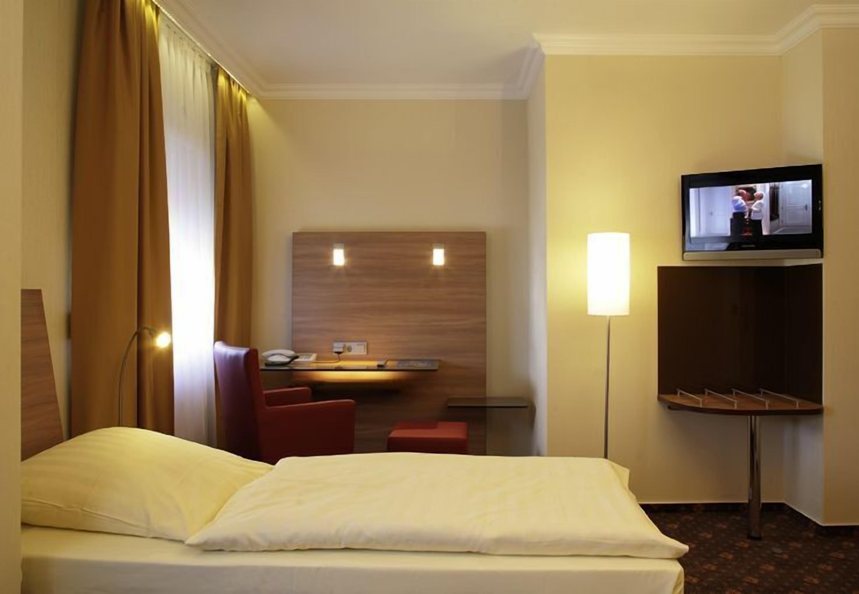 Ein Hotelzimmer mit Bett, Schreibtisch, Stuhl, Fernseher und einem kleinen Tisch mit Tablett.