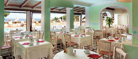 A restaurant with outdoor seating overlooking a pool and the sea.