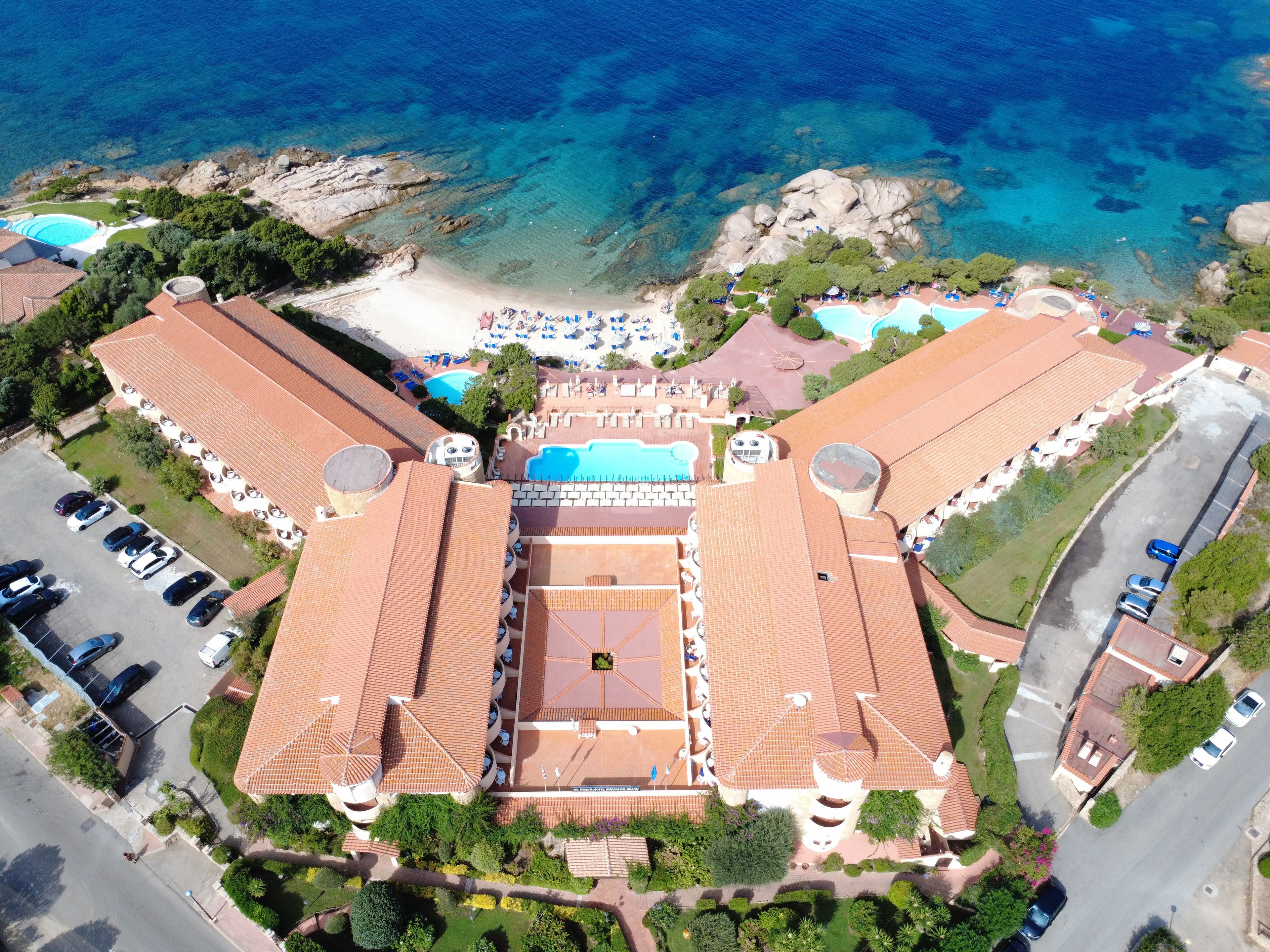 An aerial view of a resort with multiple swimming pools, a beach, and a parking area.