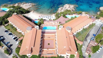 An aerial view of a resort with multiple swimming pools, a beach, and a parking area.