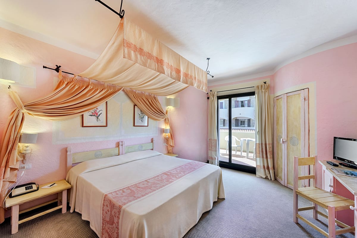 A hotel room with a bed, bedside table, lamp, and a desk with a chair.