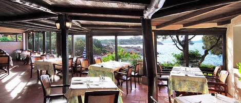 Un restaurant en plein air, avec des tables et des chaises, offrant une vue panoramique sur la mer.