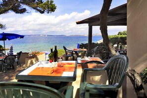 An outdoor dining area with tables and chairs, overlooking a body of water. - Grand Hotel Smeraldo Beach (Arzachena)