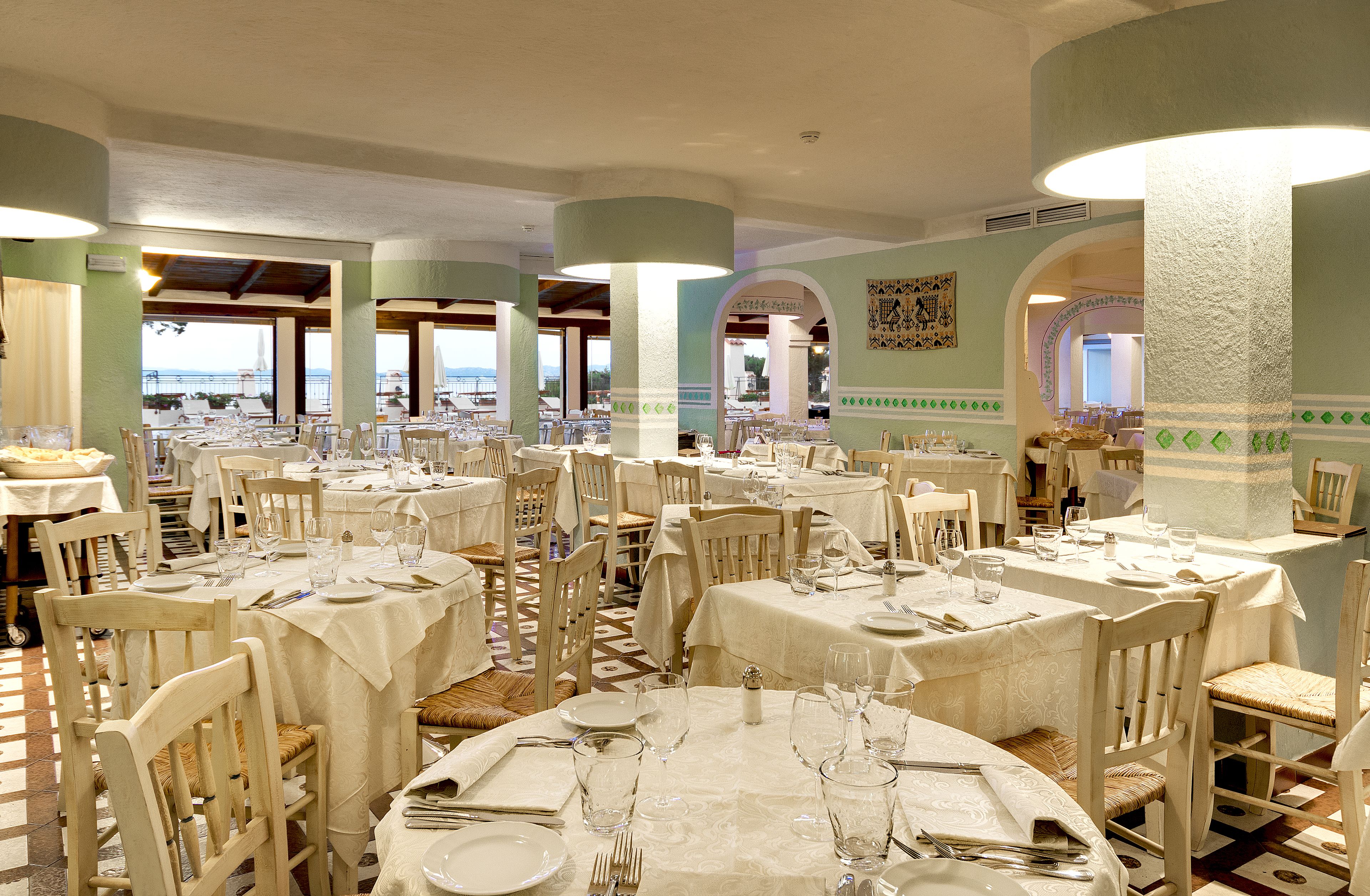 Comedor con mesas redondas dispuestas para varios comensales, con vista al mar a través de amplias ventanas.