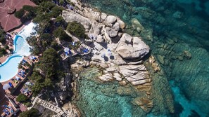 An aerial view of a coastal resort with a swimming pool, sun loungers, and clear turquoise waters. - Grand Hotel Smeraldo Beach (Arzachena)