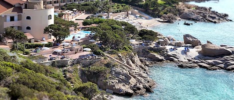 Un hôtel situé sur la côte, doté d’une piscine, d’une plage et d’un terrain rocheux.