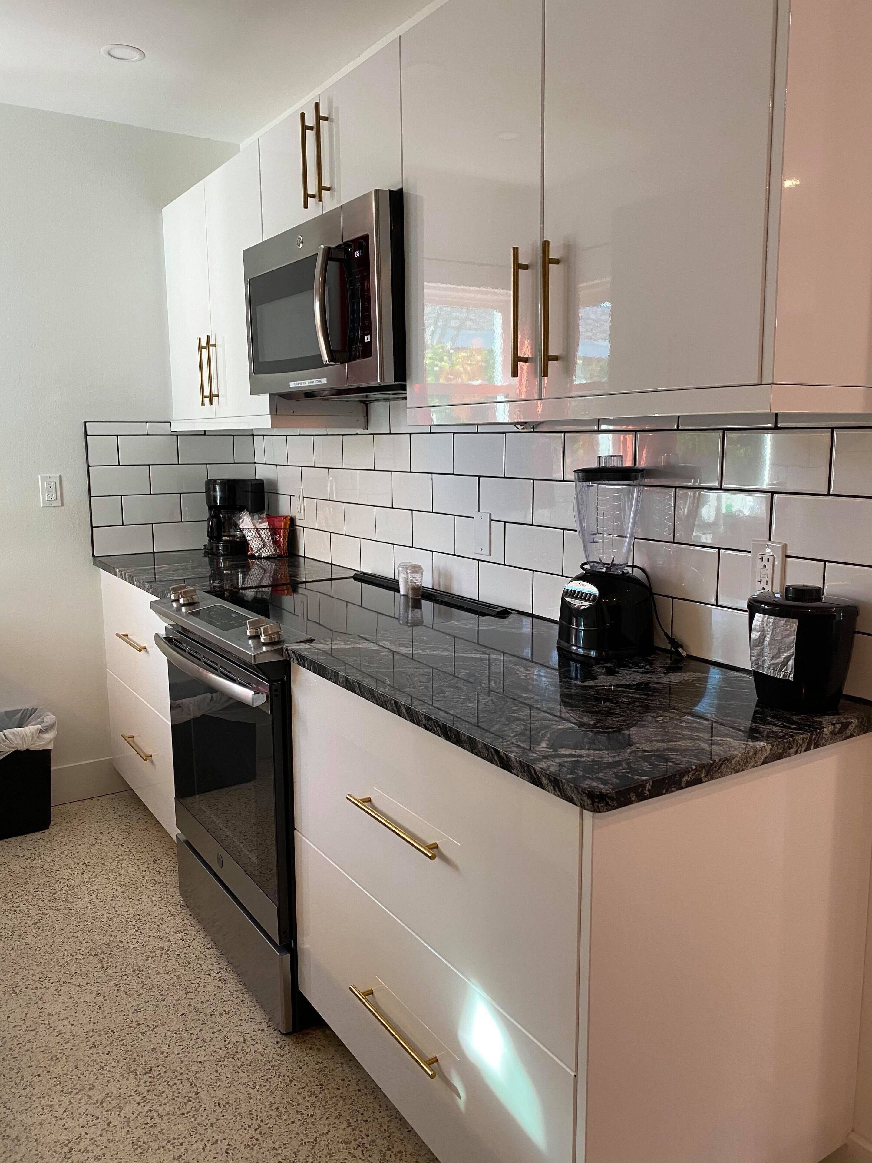 A modern kitchen with white cabinets, a black countertop, and stainless steel appliances including a microwave and oven.
