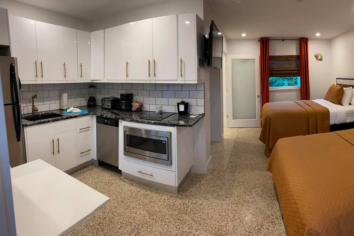A compact hotel room with a kitchenette, two beds, and a bathroom.
