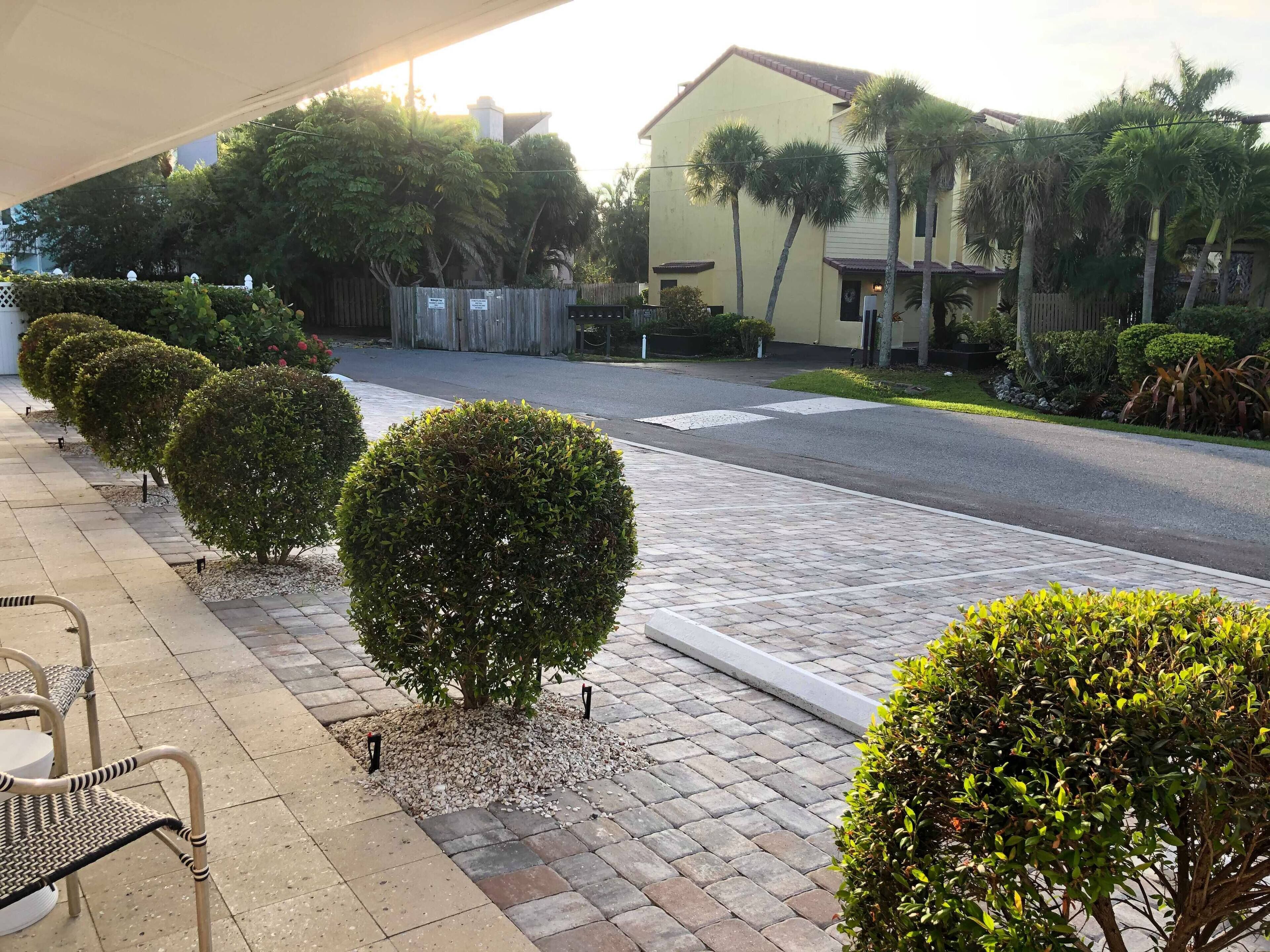 Vista de una calle con arbustos bien cuidados, una acera pavimentada y un edificio de fachada amarilla.