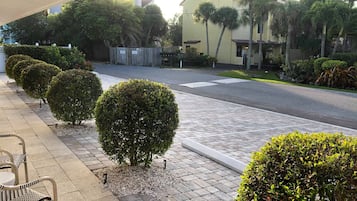 Vista de una calle con arbustos bien cuidados, una acera pavimentada y un edificio de fachada amarilla.