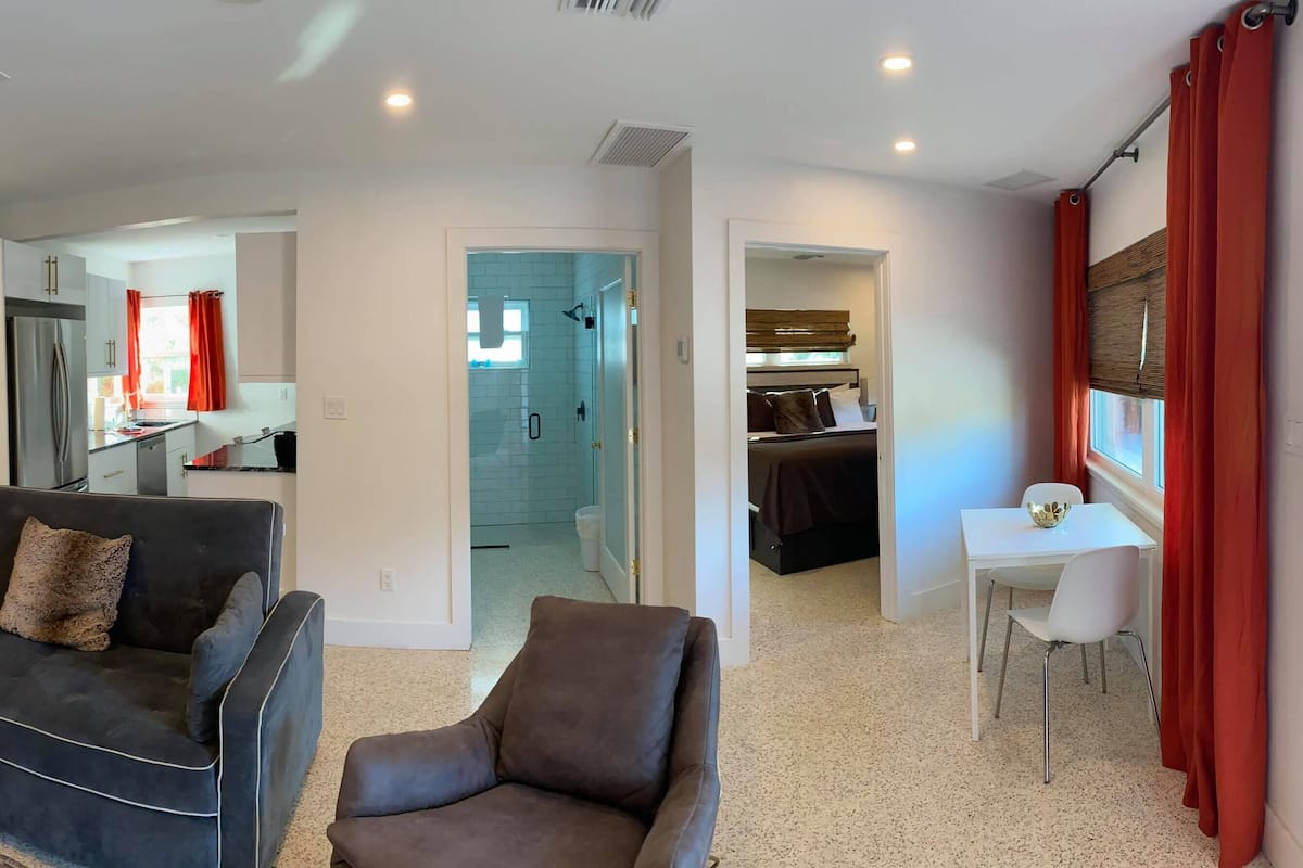 A modern living room with a sofa, armchair, and a dining area with a table and chairs.