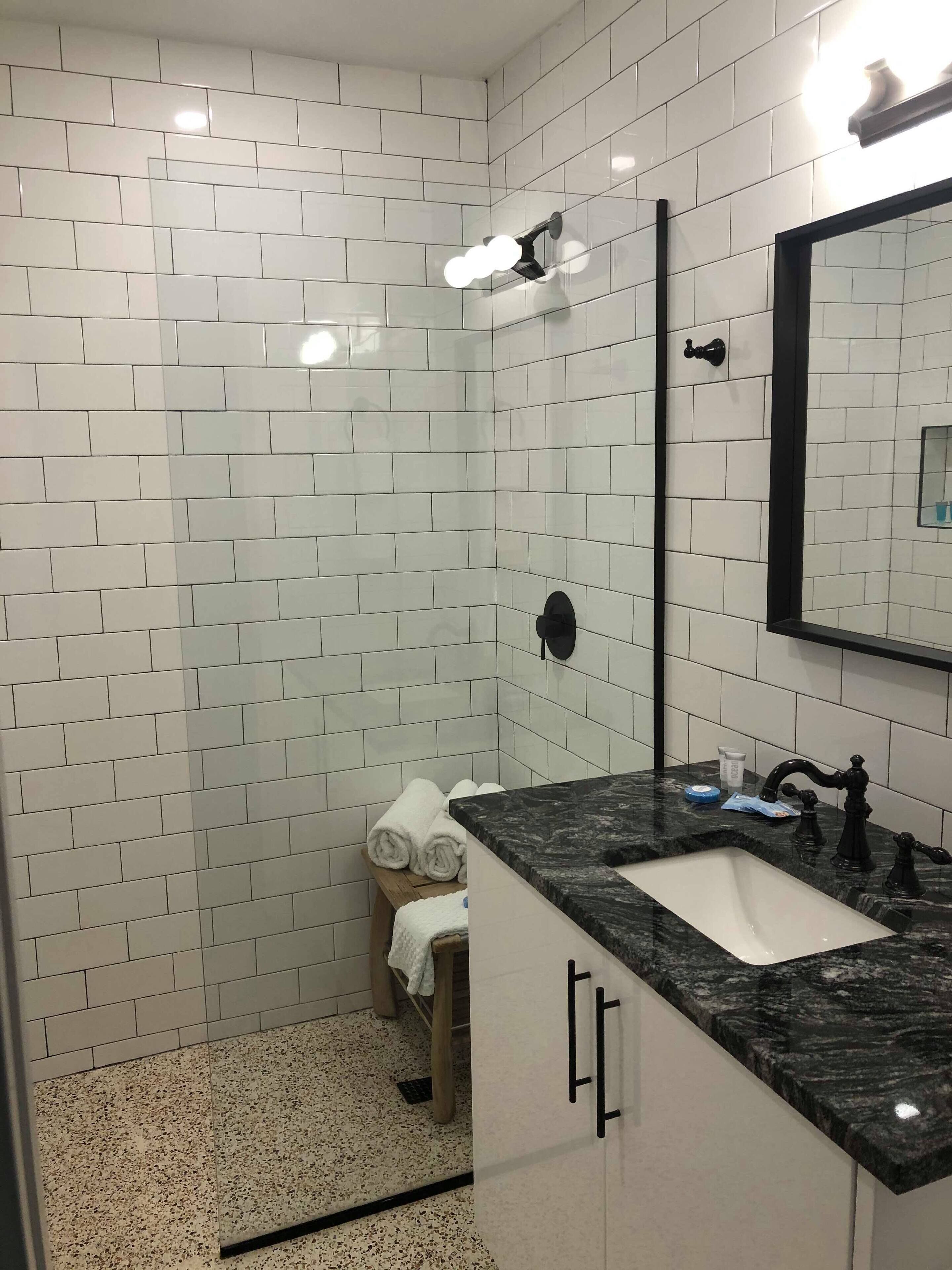 A modern bathroom with white subway tiles, a black marble sink, and a large mirror.