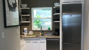 A modern kitchen with a stainless steel refrigerator, a window with a view of greenery, and a countertop with various kitchen items.