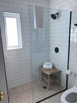 Um chuveiro com porta de vidro, um pequeno banco de madeira e uma toalha pendurada na parede.
