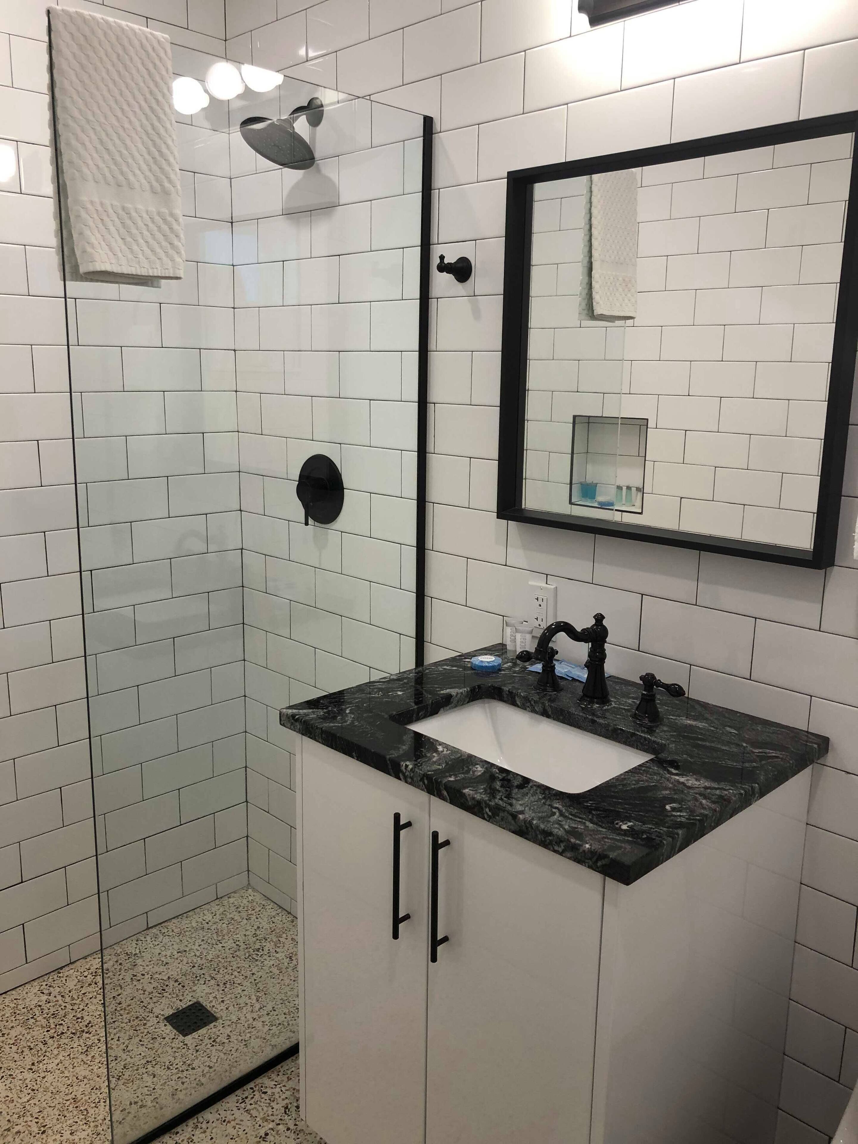 A modern bathroom with white subway tiles, a black marble sink, and a glass-enclosed shower.