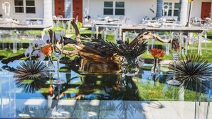 Una mesa de comedor con cristalería y ramas decorativas, ubicada al aire libre con una casa al fondo.