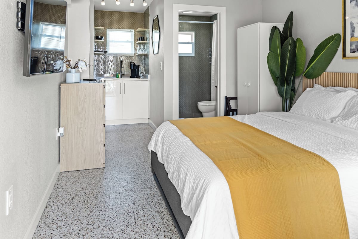 A bedroom with a bed, a wardrobe, a bathroom, and a kitchenette.
