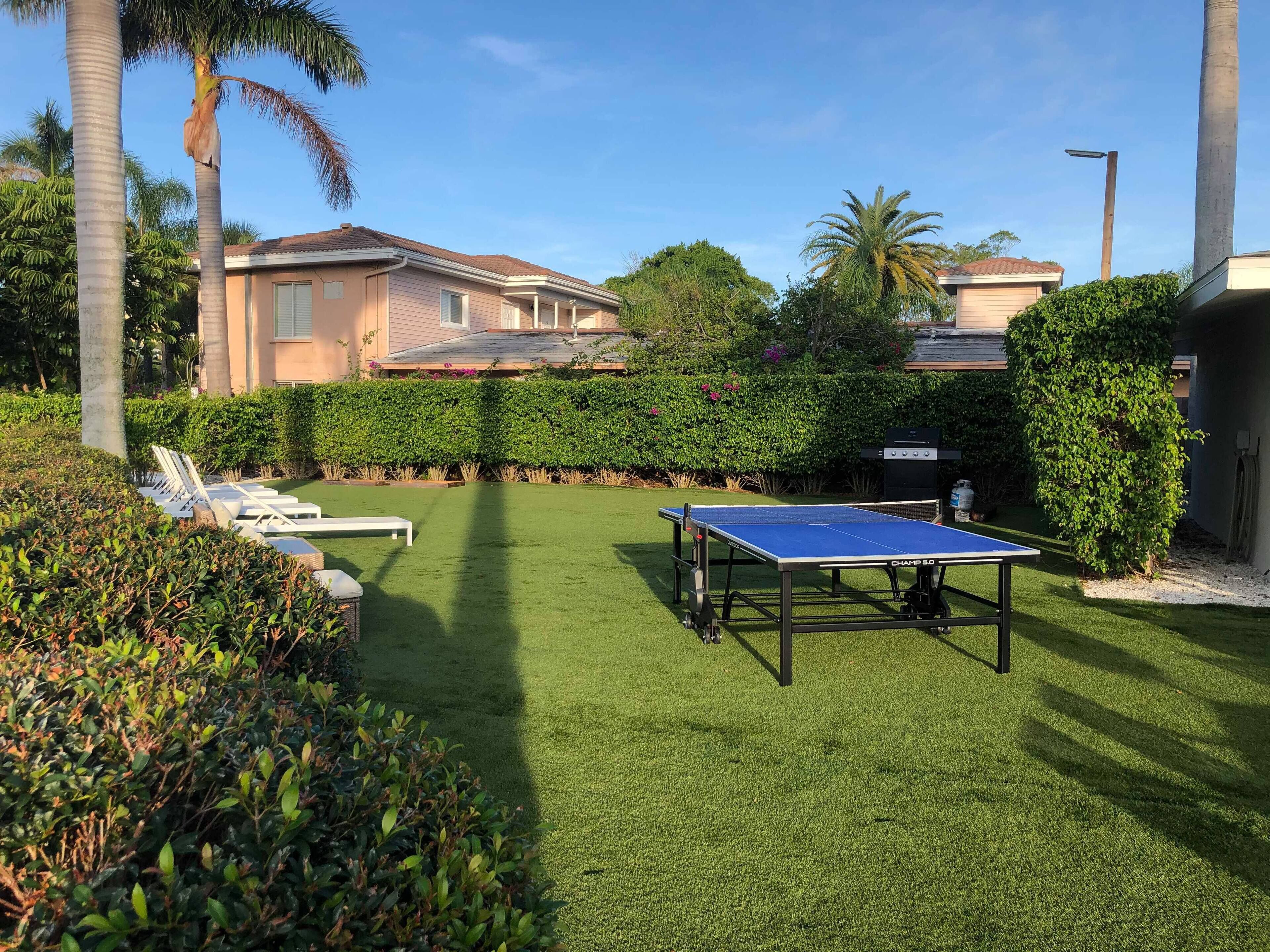 A well-maintained outdoor area with a ping pong table, lounge chairs, and a neatly trimmed hedge.