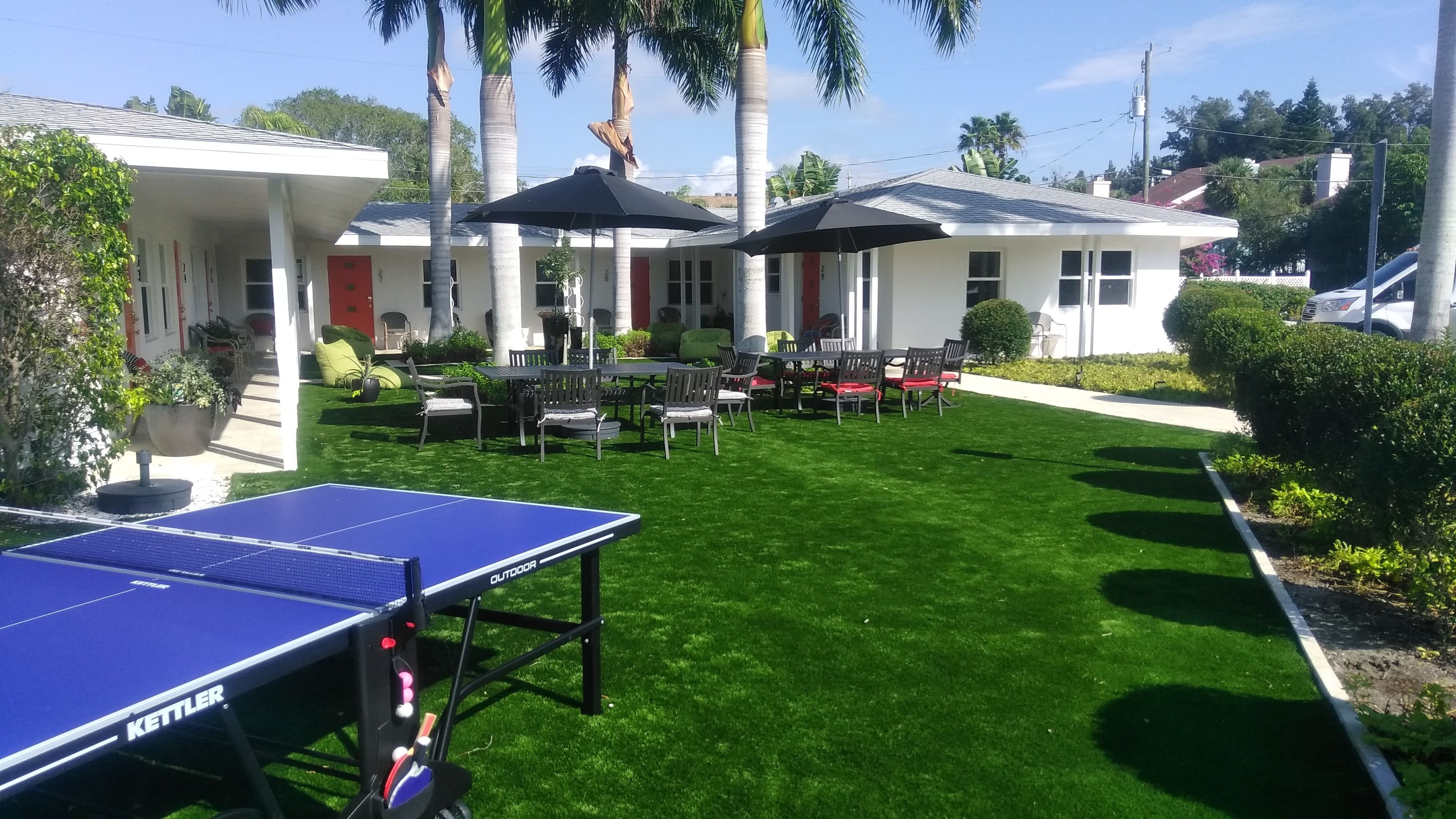 An outdoor patio area with a ping pong table, outdoor seating, and palm trees.