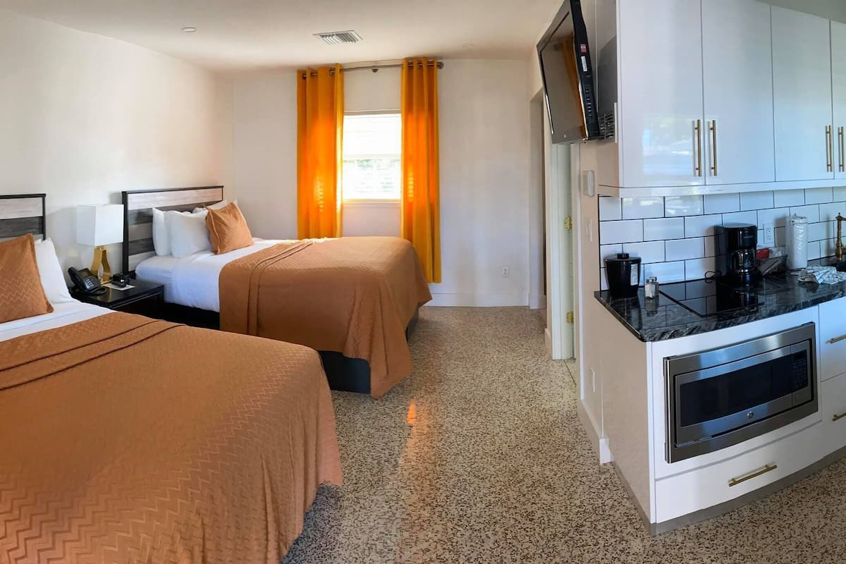 A hotel room with two beds, a kitchenette, a dining area, and a TV.