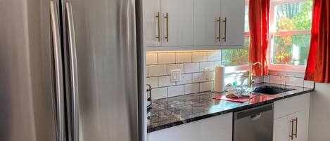 A modern kitchen with white cabinets, stainless steel appliances, and a marble countertop.