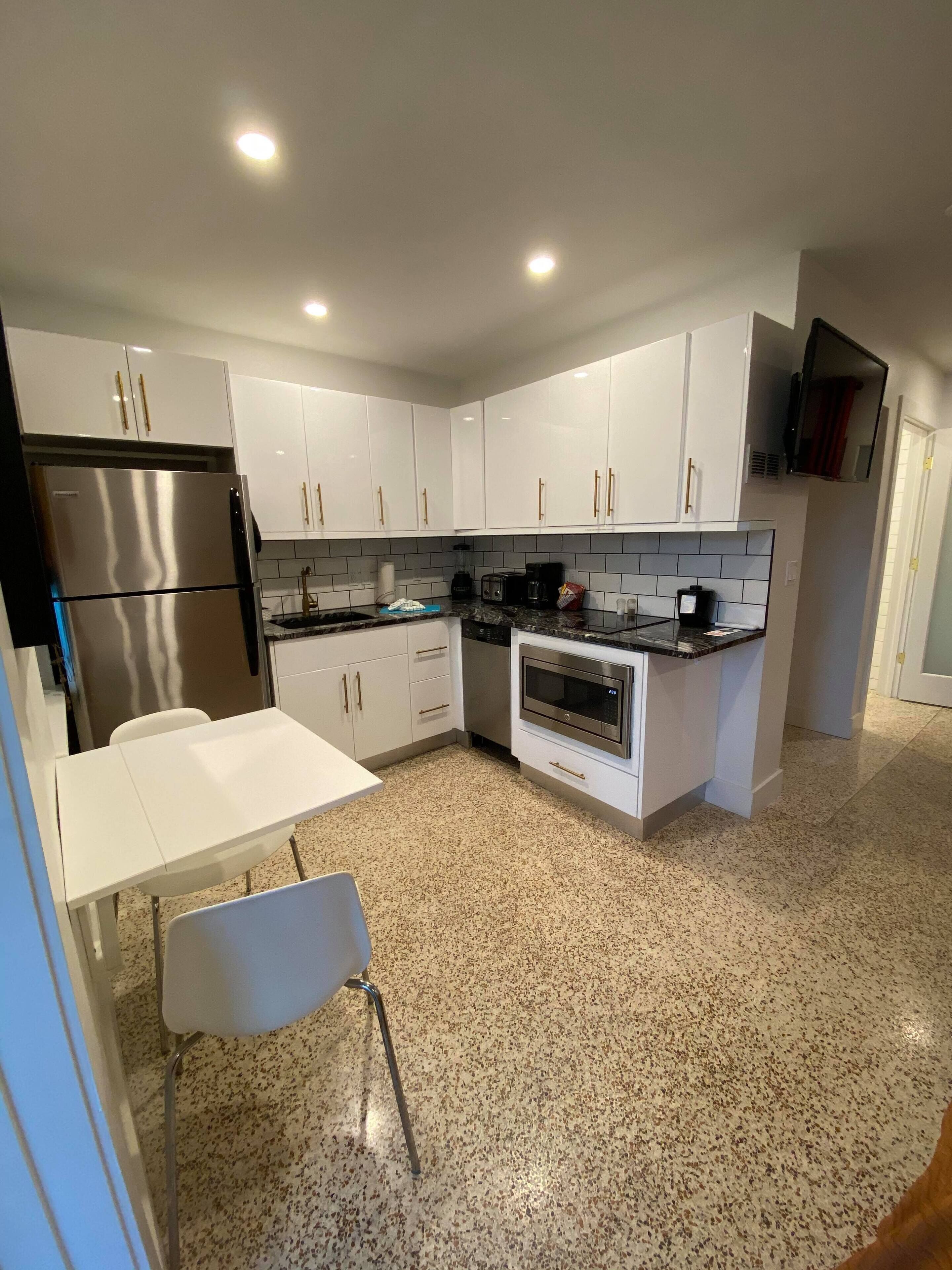 A modern kitchen with white cabinets, a stainless steel refrigerator, a built-in oven, and a granite countertop.