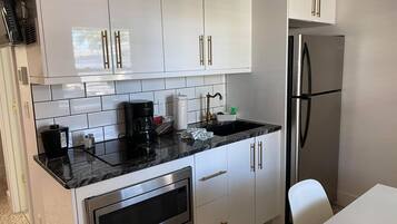 Ett modernt kök med vita skåp, ett kylskåp i rostfritt stål, en inbyggd mikrovågsugn och en svart bänkskiva.