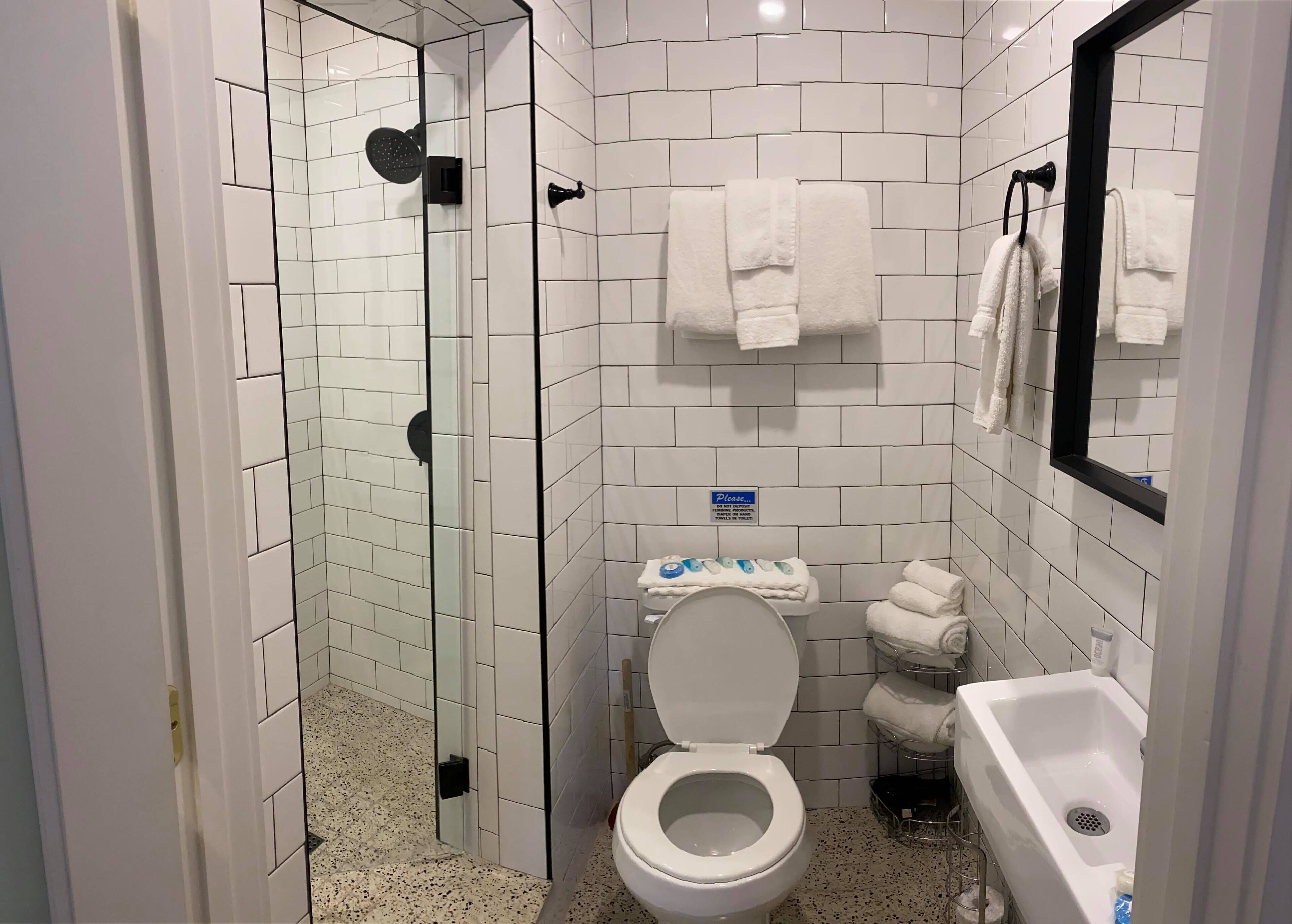 Egy fürdőszoba zuhanyzóval, WC-vel, mosdókagylóval és törölközőtartóval.