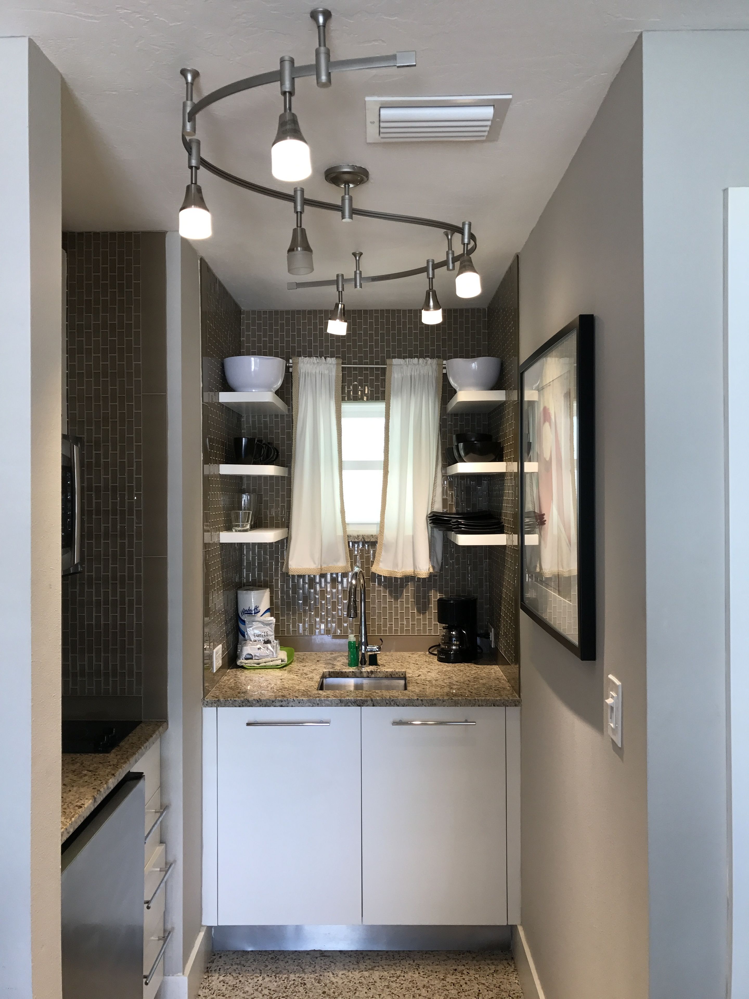 A modern kitchen with white cabinets, a granite countertop, a coffee maker, and a hanging light fixture.